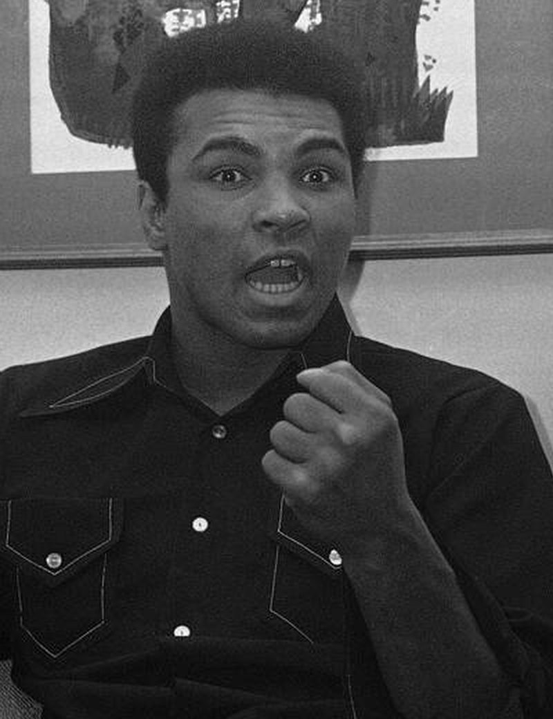 A boxer in a dark shirt talking animatedly with a raised fist, mid-sentence.