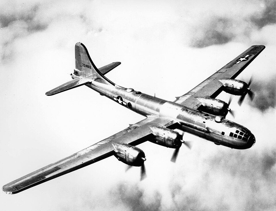 A large four-engined bomber with a glazed nose photographed from above in flight over cloud.