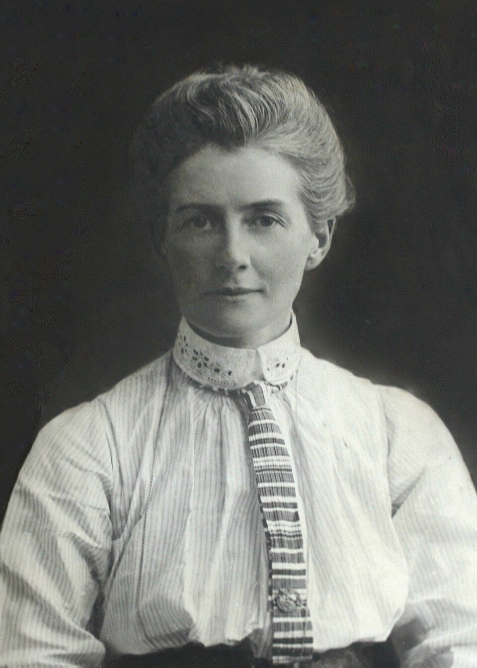 A formal photograph of a woman with pinned-up hair in a high-collared white blouse, looking calmly past the camera.