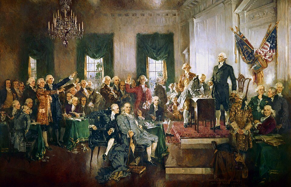 A large painting of dozens of men in eighteenth century coats and breeches gathered in a hall, one standing on a dais beside a draped flag.