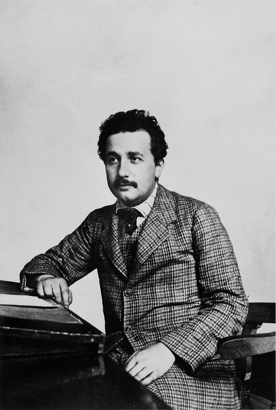 A formal photograph of a young man with dark hair and a moustache in a suit and high collar.