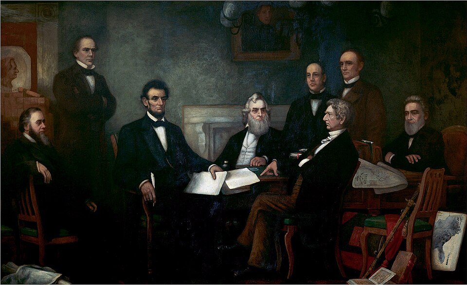 A painting of a tall man seated at a table reading from a document to a group of seated and standing men in a formal room.