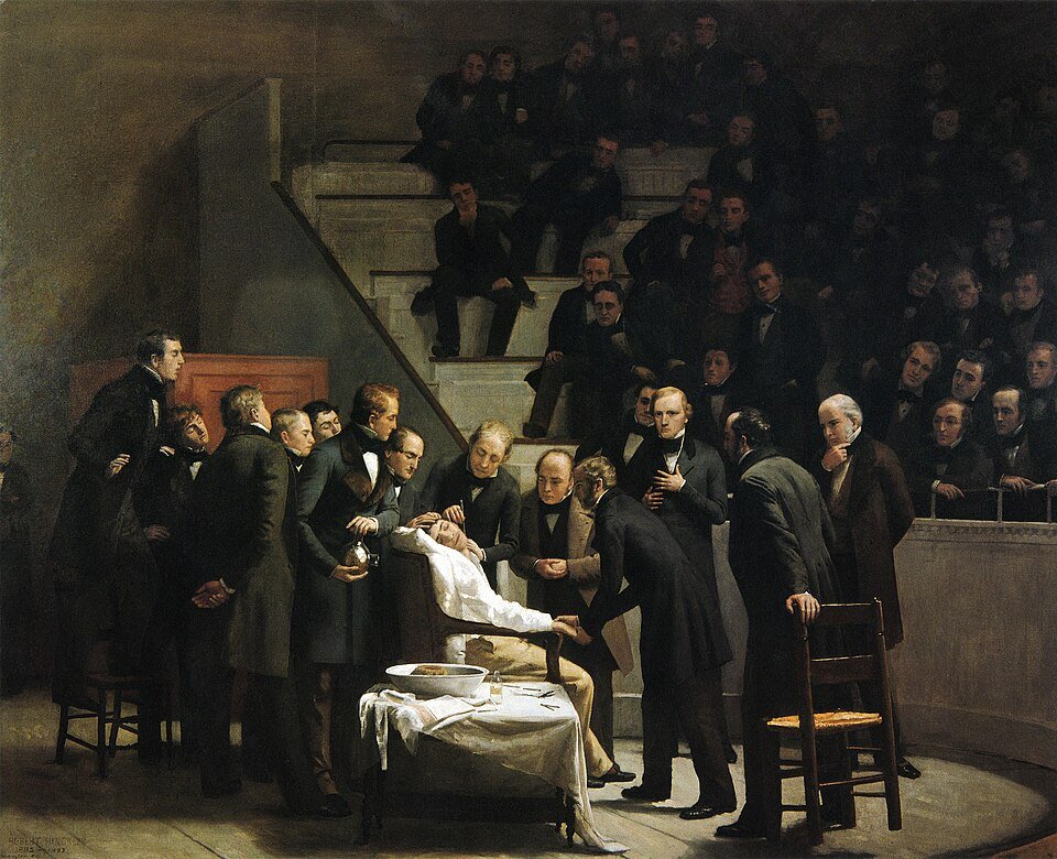 An oil painting of a surgical theatre, a patient lying on a table under a sheet surrounded by men in black frock coats, with tiers of onlookers watching from behind.