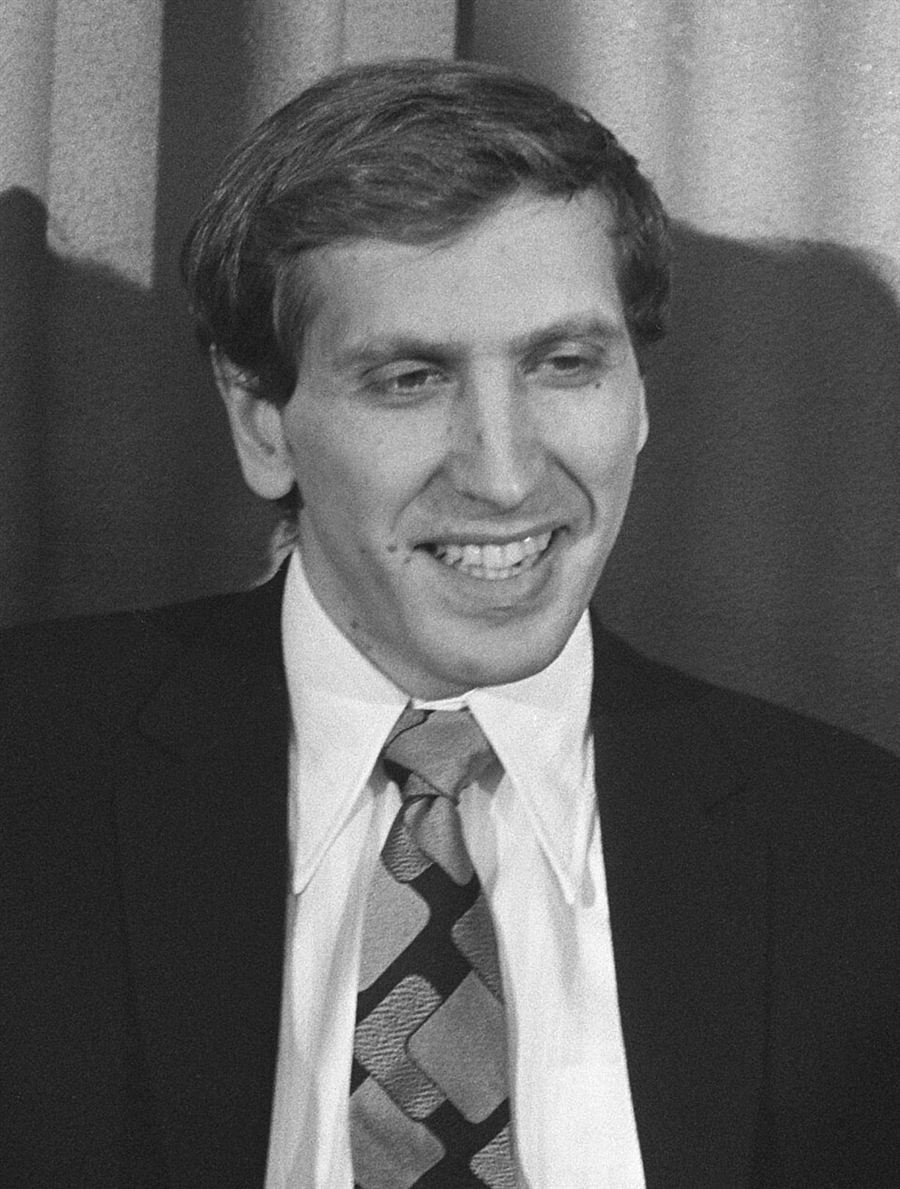 Black and white portrait of a smiling young man in a dark suit and wide collared shirt.