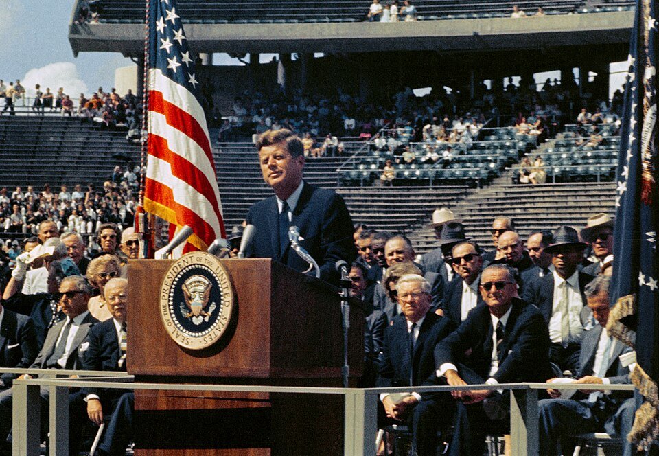 Colour photograph of a president speaking at a podium bearing the presidential seal before a stadium crowd.