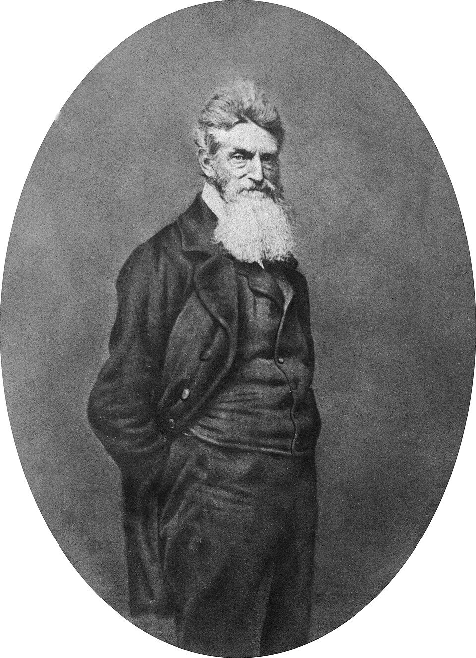 An oval photographic portrait of a gaunt man with a long white beard and severe expression, in a dark coat, arms at his sides.