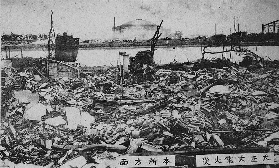 Black and white photograph of a vast field of rubble and burnt debris stretching to a river, with Japanese characters printed along the bottom edge.