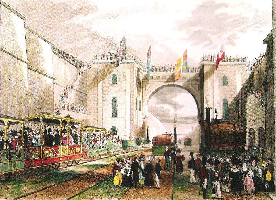 A coloured engraving of early trains of open carriages passing under a stone arch hung with flags, crowds watching from above.