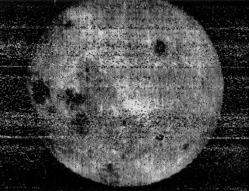 A grainy black and white image of a bright, heavily streaked lunar disc against a noisy dark background.