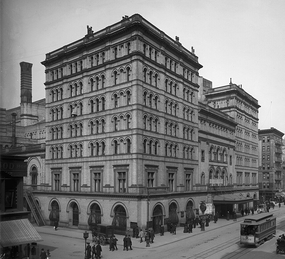 A large stone opera house of seven storeys filling a city block, with rows of arched windows, awnings at street level and a tram passing in front.