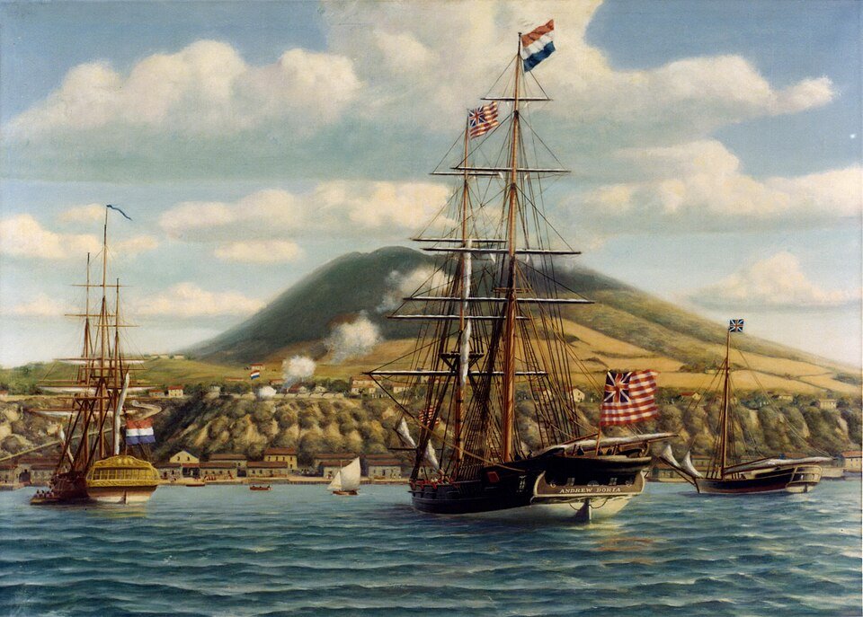 An oil painting of a black-hulled sailing brig at anchor in a bay under a striped flag, with a fort and a green hillside town behind and smoke drifting from a salute.