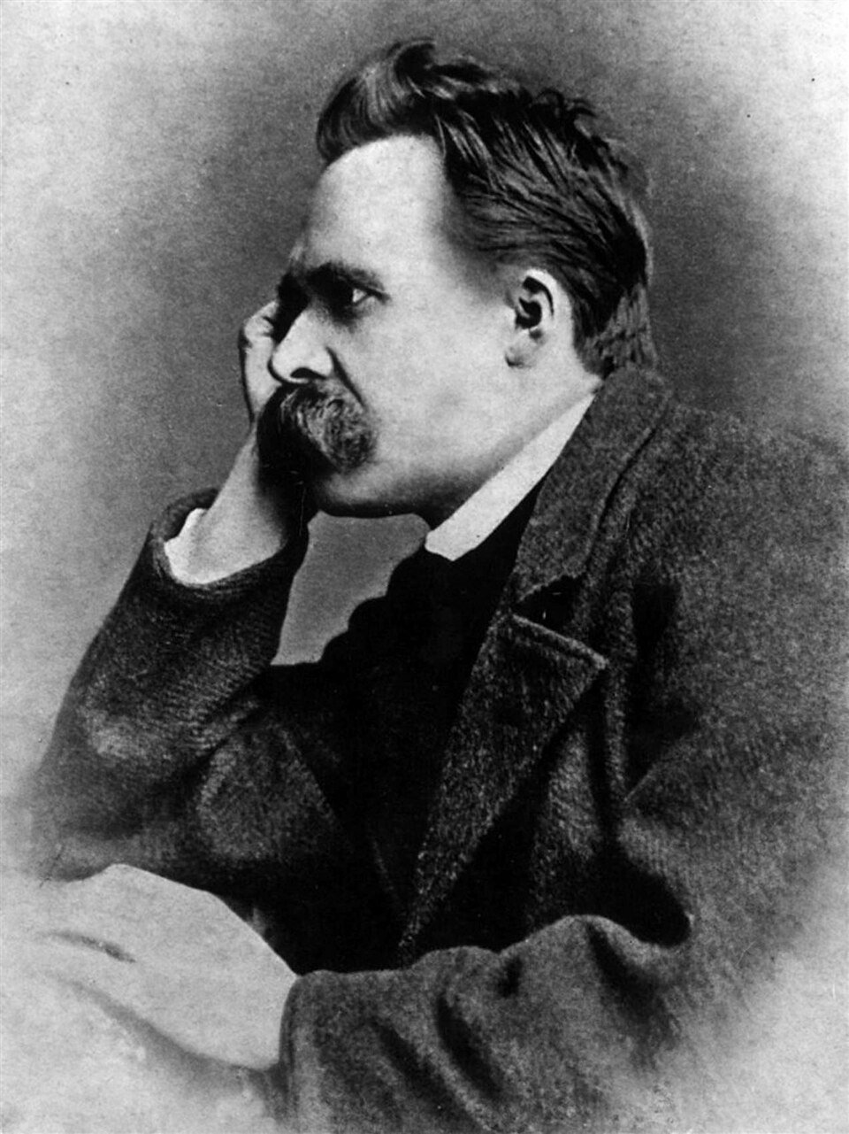 A photographic portrait of a man with a very large drooping moustache and dark swept-back hair, resting his head on one hand, in a heavy coat.