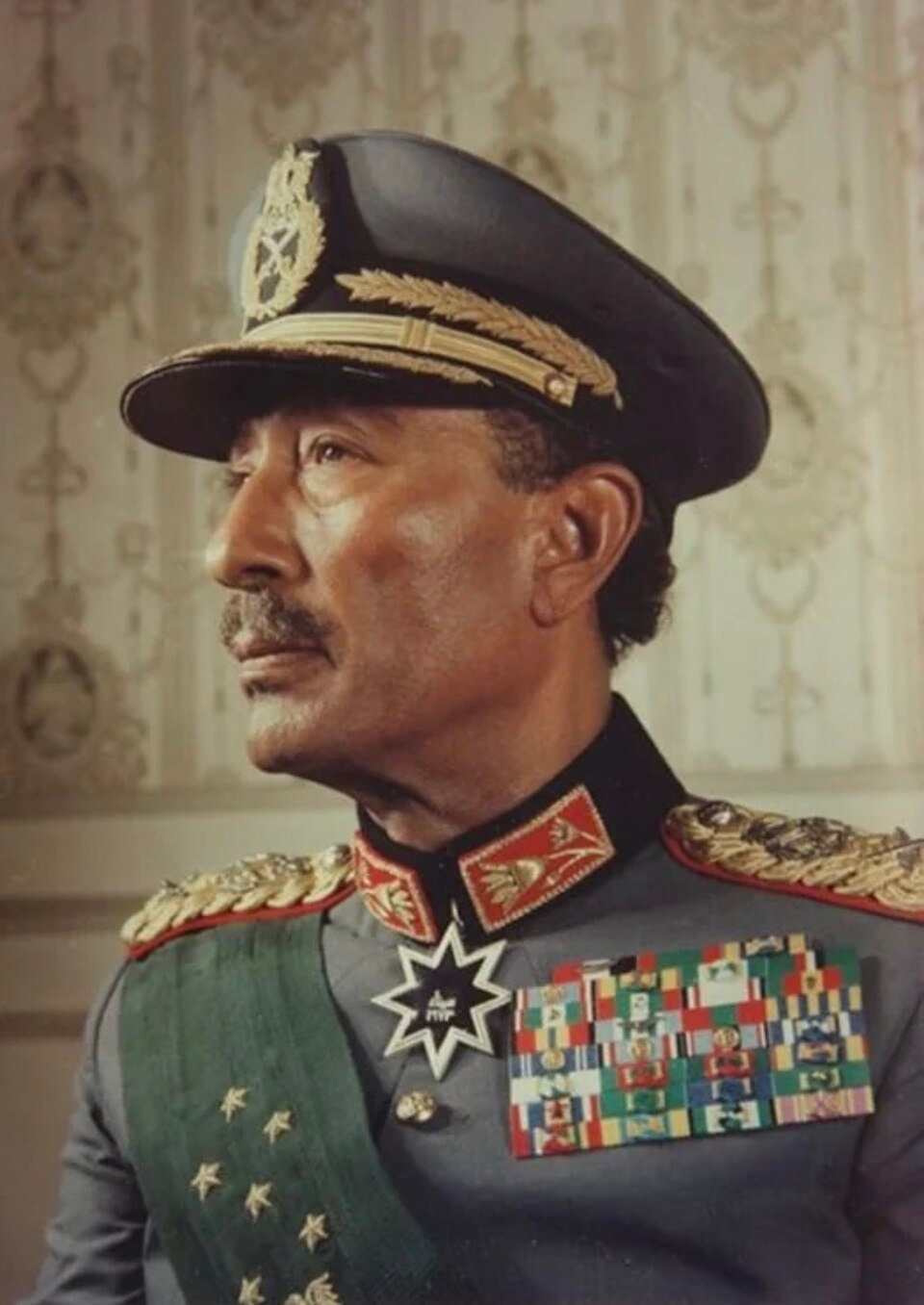 A colour portrait in profile of a man in a grey dress uniform with gold epaulettes, a row of medal ribbons and a peaked cap.