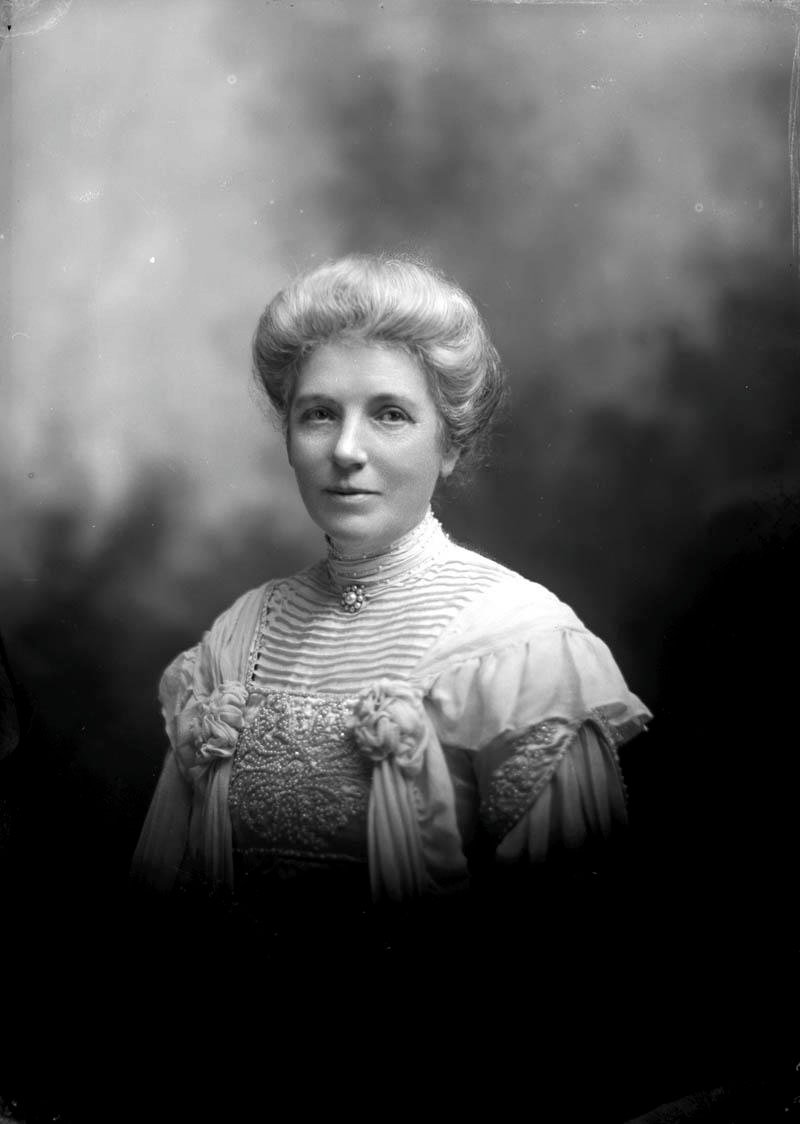 A studio photograph of a woman with swept-up grey hair in an embroidered high-necked blouse.