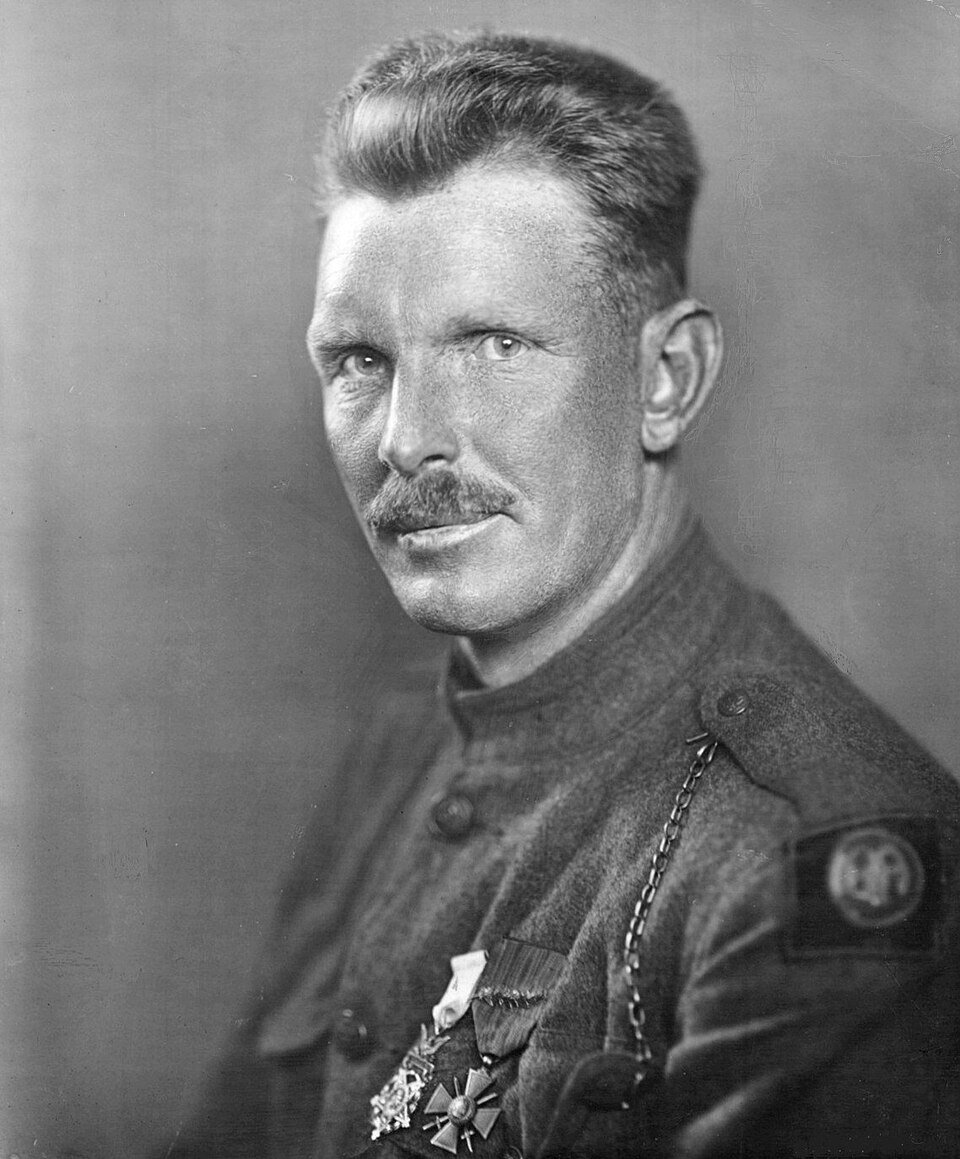 A portrait of a soldier in a high-collared tunic with a divisional patch on the shoulder and several medals pinned to his chest, looking slightly away from the camera.